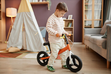 Portrait of little boy with down syndrome learning to use runbike indoors