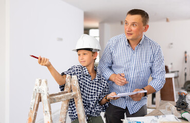 Father and his young son discussing work plan in construction site in apartment, making pointing finger gesture.