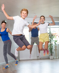 Fototapeta na wymiar Friendly sporty parents with teen daughter and son jumping up high during dance training together in wellness studio. Family health concept