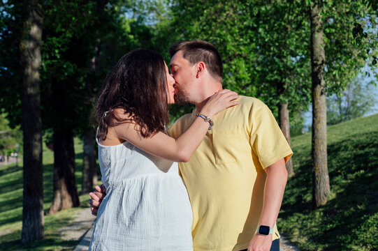 Married couple in expectance kissing in green park