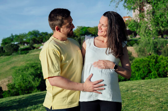 Happy couple in expectance embracing standing in park