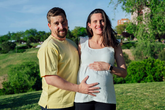 Happy couple in expectance embracing standing in park