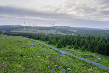 Aerial view on a wind farm turbine build in a rural country area with green forest. Making power using power of nature. Blending technology into nature environment. Cloudy sky. Electricity production