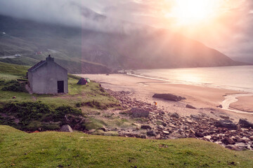 Small house by the ocean and beach, sun rise over a cliff and low cloudy sky. Keem beach, Ireland....