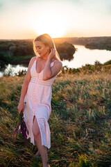 beautiful slim young woman posing on nature background in summer at sunset full-length. female is relaxing in the field with flowers. 