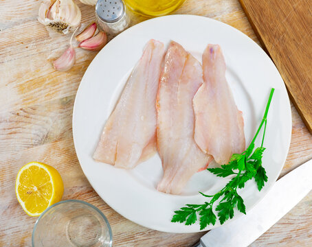 Raw fish with condiments, red perch fillet on plate with garlic and parsley on wooden surface