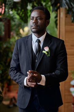 Vertical portrait of handsome black man getting ready for wedding ceremony and adjusting tux
