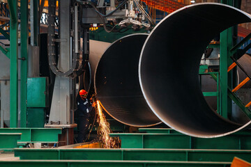 Worker cleans welded seam on steel pipe using grinding machine