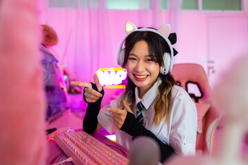 Young Asian woman esport player playing online game on computer in bedroom. Attractive girl vlogger influencer gamer enjoy and fun live streaming broadcast games challenge on social media platform.