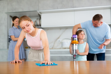 Teenage girl actively participating in household chores by assisting family in cleaning apartment,...
