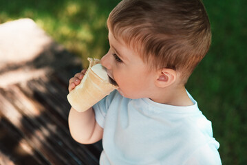 A cute little European-looking kid is eating an ice cream cone in a waffle cup in the park....
