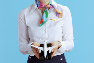 Female stewardess on blue showing little airplane and smartphone