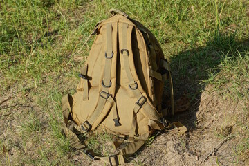 one brown army backpack stands on gray ground and green grass in the street