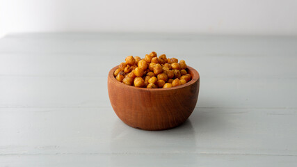 Close view of a wooden bowl filled with salty crispy chickpeas. over a white wooden table
