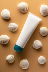 Plastic tube with sunscreen cream on beige background with seashells.