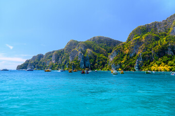 Fototapeta premium Boats and ships in the bay of Ko Phi Phi Don Island with huge rocks and cliffs on a sunny day, Ao Nang, Mueang Krabi District, Krabi, Andaman Sea, Thailand