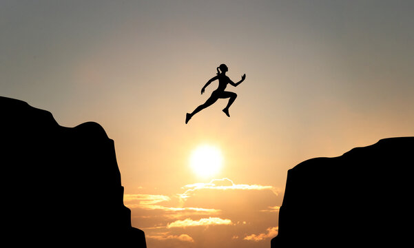 Concept of reaching life and business goals. Silhouette of woman jumping over chasm at sunrise