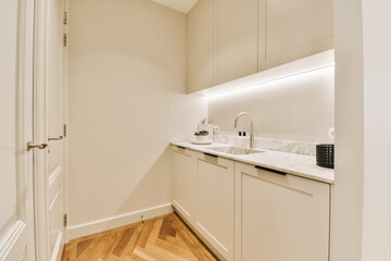 a kitchen with white cupboards and wood flooring in the middle of the room there is a microwave on the wall