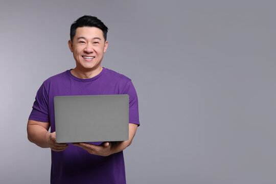 Happy man with laptop on grey background, space for text