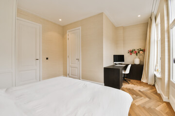 a bedroom with wood flooring and white sheets on the bed, there is a small desk in front of the window