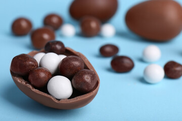 Tasty chocolate egg with different sweets inside on light blue background, closeup. Space for text