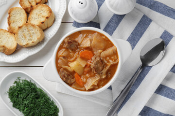 Tasty cabbage soup with meat and carrot served on white wooden table, flat lay