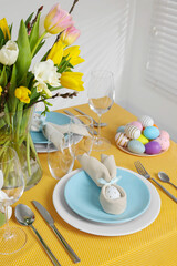 Festive table setting with painted eggs, cutlery and vase of tulips. Easter celebration