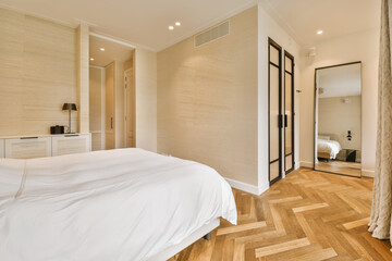 a bedroom with wood flooring and white sheets on the bed, in front of a mirror that is hanging above it