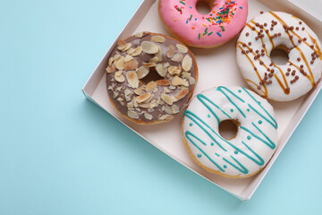 Box with different tasty glazed donuts on light blue background, top view