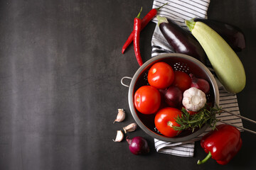 Cooking delicious ratatouille. Fresh ripe vegetables and colander on dark grey table, flat lay....