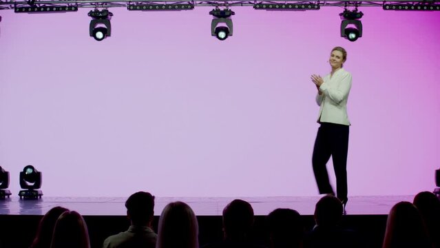 Caucasian woman female speaker presenting on the stage during conference. Presenting ideas against bright pink background