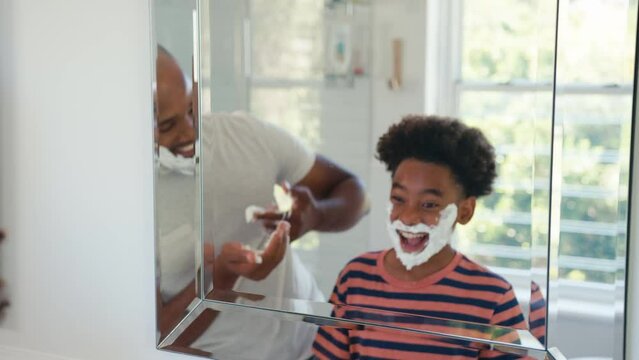 Father and son at home having fun playing with shaving foam in bathroom making a mess together - shot in slow motion