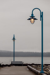 deux lampadaires en métal bleu avec abat jour sur le bord d'une rue au bord du fleuve