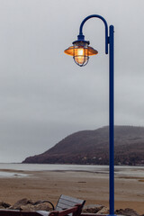 lampadaire en métal bleu avec abat jour sur le bord d'une rue au bord du fleuve avec une colline en arrière plan