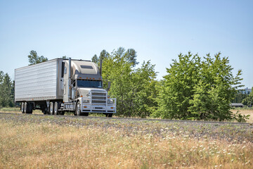Beige big rig bonnet classic semi truck with grille guard transporting cargo in refrigerator semi...