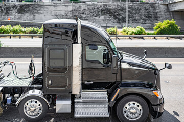 Stylish high cab black big rig semi truck tractor with semi trailer driving on the highway road