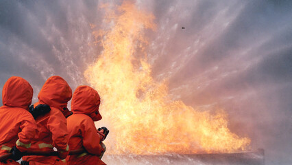 Firefighter Rescue team training in fire fighting extinguisher. Firefighter teamwork fighting with flame using fire hose chemical water foam spray engine. Fireman wear hard hat, safety suit uniform