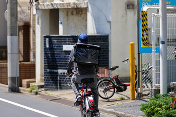 街中の道を自転車でフードデリバリーする男