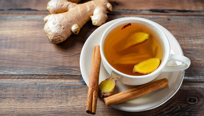 Cup of tea with ginger and cinnamon on wooden background