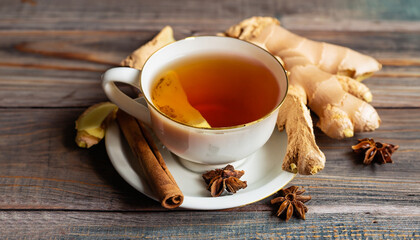 Cup of tea with ginger and cinnamon on wooden background