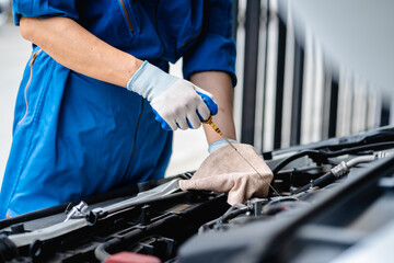 Obraz premium Close up, Auto mechanic repairman using tablet and pulling dipstick to checking engine oil level engine in the engine room, check the mileage of the car, oil change, auto maintenance service concept.