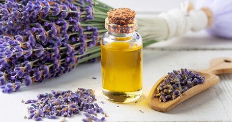 Glass bottle of Lavender essential oil with fresh lavender flowers and dried lavender seeds on white wooden rustic table, aromatherapy spa massage concept. Lavendula oleum