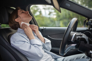 Woman drives car with broken air conditioning in hot summer weather wipes sweat paper napkin. Middle aged female suffering from heat stuffiness. Tired exhausted overheated stressed worried driver. - obrazy, fototapety, plakaty