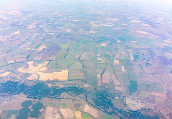 Fototapeta premium Aerial view from airplane window above green ground. View from the airplane window with beautiful clouds at sunrise