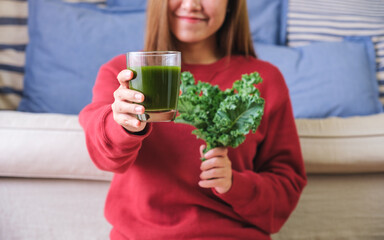 Closeup image of a young woman holding and showing kale leaves and kale smoothies