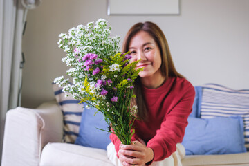 Portrait image of a beautiful young asian woman holding flower bouquet at home