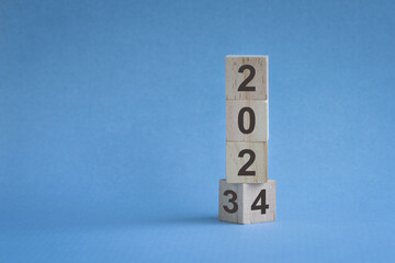 Wood cubes or blocks stack on table, turn of year from 2023 to 2024. On blue background.