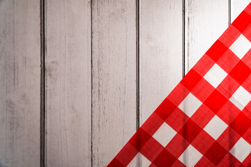 Fototapeta na wymiar A top lay photo of a wooden picnic table with a red and white checked tablecloth folded diagonally across the right third of the frame. The photo leaves plenty of room for ad copy.