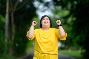 Asian woman with down syndrome doing winner pose with her arms raised Smiling and screaming for success in a natural park