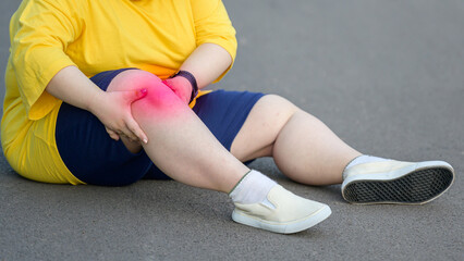 Fat young woman sits with sore legs and knees from running or sore knees from exercising in the park